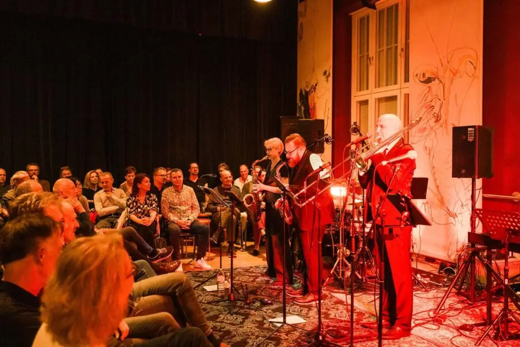 Die Band spielt in einem Saal mit verzierten Wänden, das Publikum sitzt dicht davor