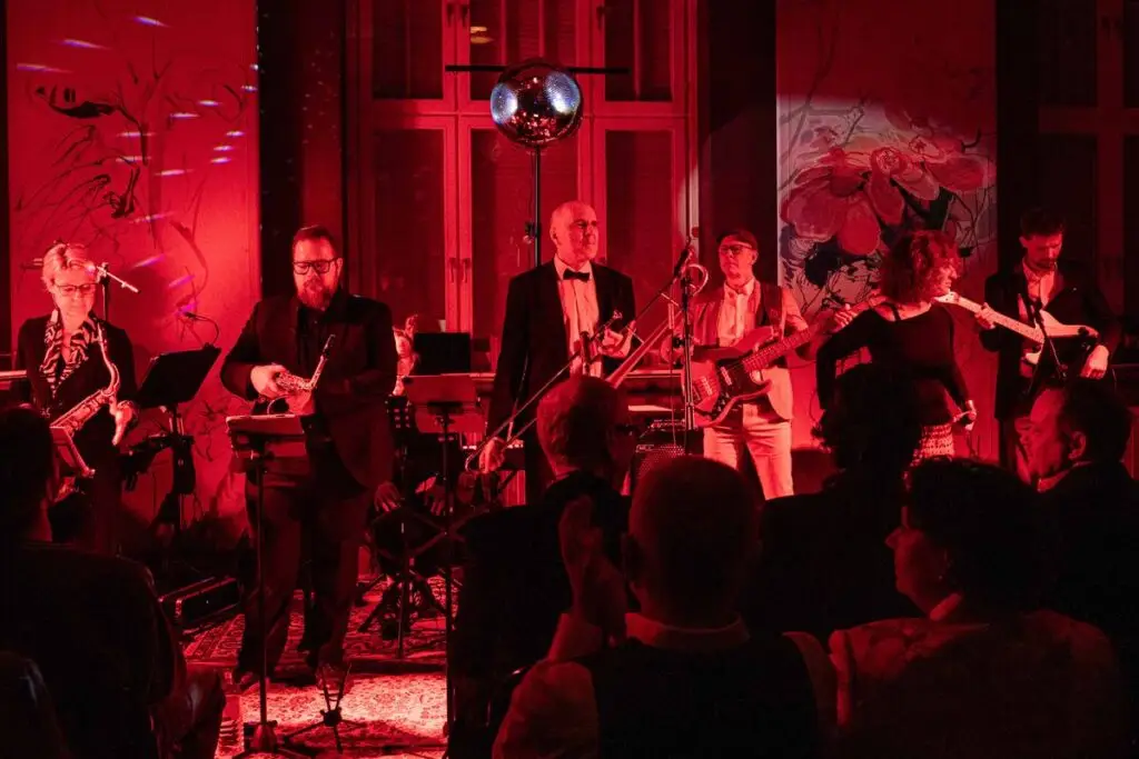 Die Band spielt auf einer privaten Feier in rotem Licht, Gäste stehen direkt vor den Musikern