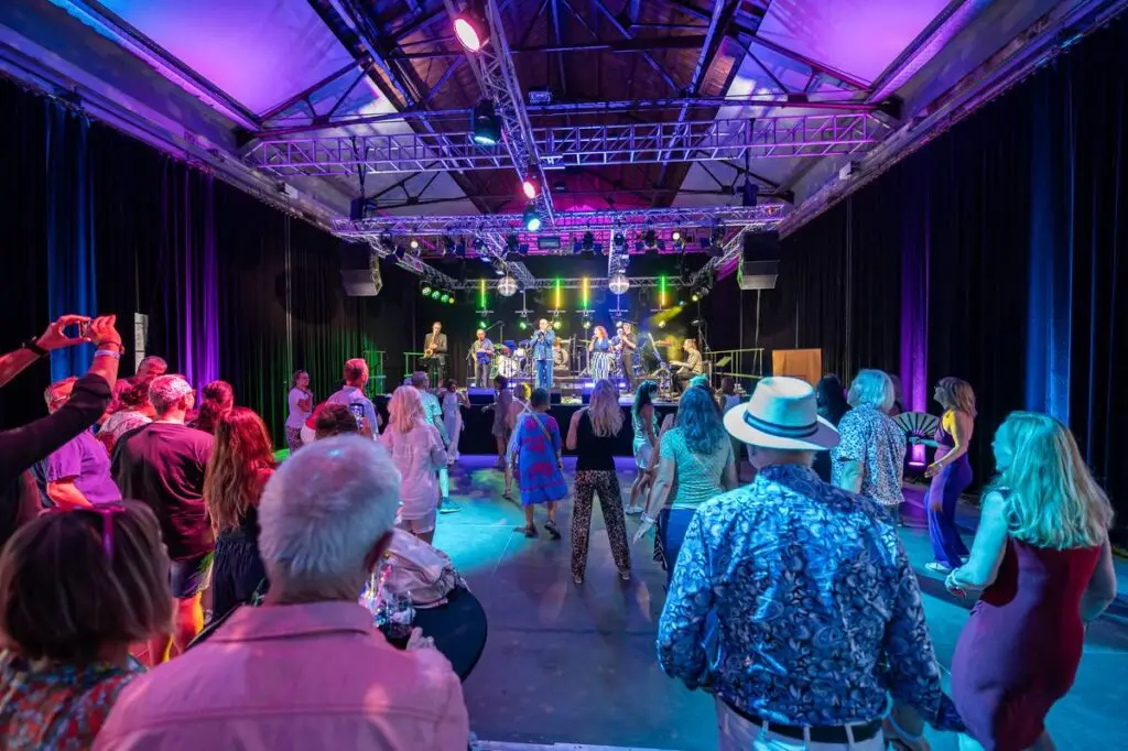 Dicht gedrängtes Publikum tanzt in einer Halle unter buntem Bühnenlicht